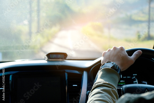 Man sit in the car hand is driving the car on the road. travel to He is looking to a road traffic route and listening to music happily .