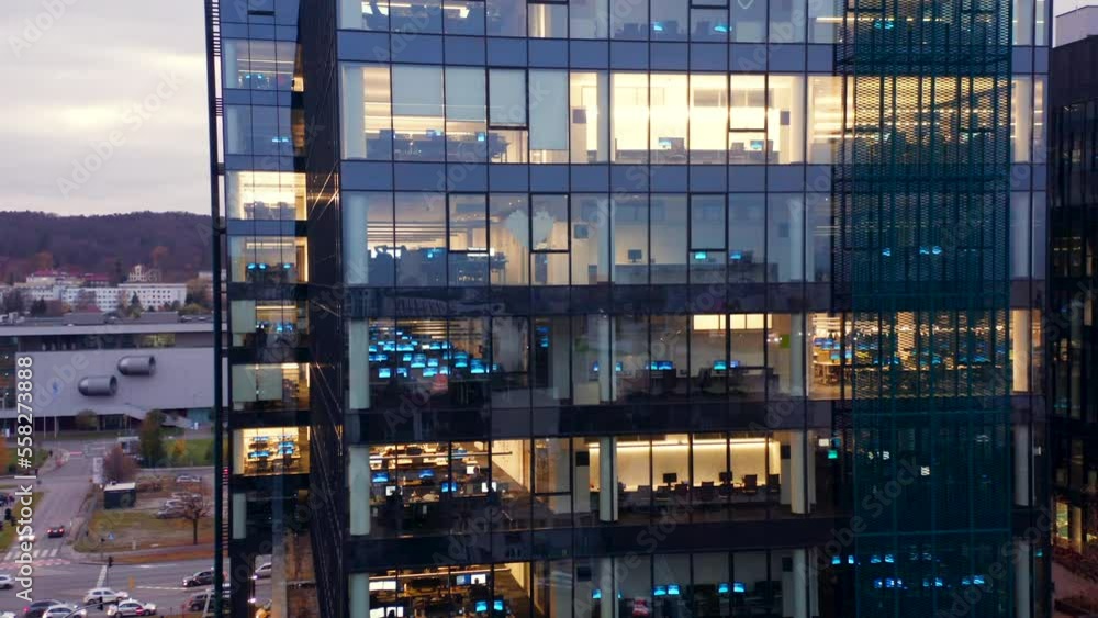 Skyscraper at dusk. Drone shot at office windows in a skyscraper at night. Flying around the glass facade of the building with people working late. Skyscraper at dusk. Drone shot at office windows in a skyscraper at night. Flying around the glass facade of the building with people working late.