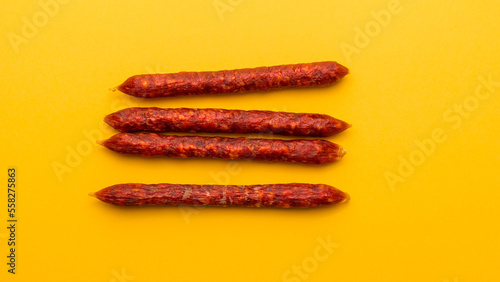 Flat lay of Snack sticks of Chorizo on the yellow background, traditional dried sausage from Spain