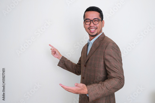 Asian businessman wearing brown suit smiling happy while pointing finger on white space behind photo