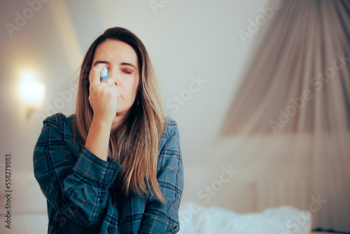 Woman Using an Asthma Inhaler Sitting in the Bedroom at Home. Asthmatic person having wheezing and breathing problems at night
 photo