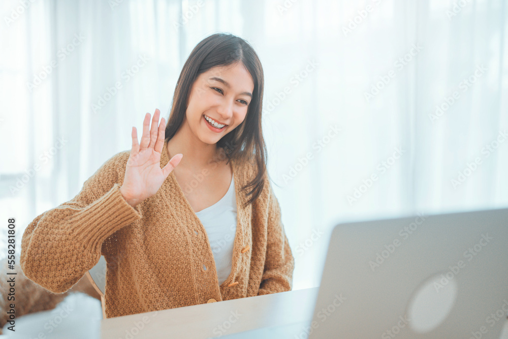 Happy positive young asian woman enjoying online communication at home, Female using wifi while video conferencing with friend, sitting in front of open laptop, smiling and waving hand, saying hi Happy positive young asian woman enjoying online communication at home, Female using wifi while video conferencing with friend, sitting in front of open laptop, smiling and waving hand, saying hi