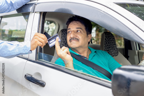Happy indian mature man sitting in car wearing seat belt give credit or debit card to fill petrol in car at gas station. Cashless Payment.