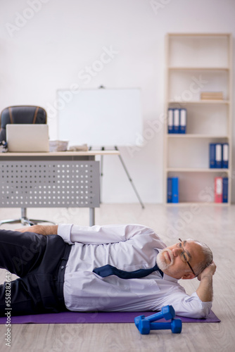 Old male employee doing sport exercises at workplace