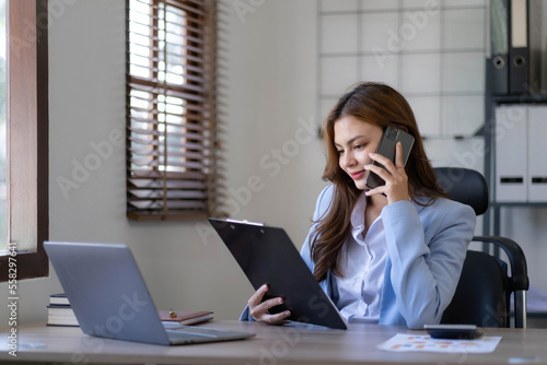 Portrait of smiling business asian woman using smartphone while sitting at workplace.