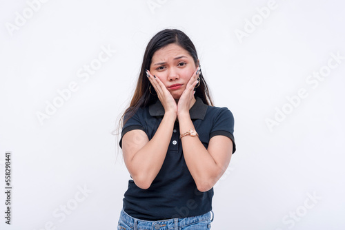 A young asian woman pouting, feeling disappointed. Squishing her cheeks with both hands. Isolated on a white backdrop. photo