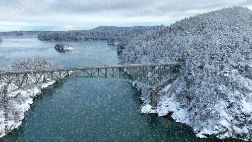 Wide shot of a bridge spanning water with snow actively falling. photo