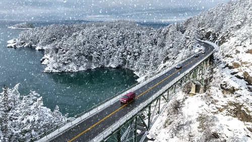 Cars driving across Deception Pass bridge with snow falling and covering the ground. photo