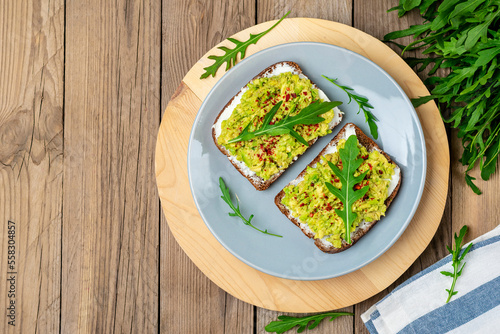 Set sandwiches for breakfast - slice of whole grain dark bread, cream cheese, guakomole, garnished with arugula, paprika on wooden table Top view Flat lay Healthy food concept Homemade