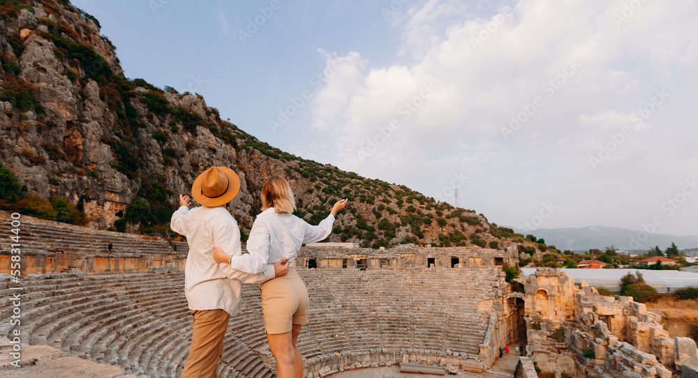 Fototapeta premium Happy lover couple tourist archaeologist in hat background old tomb Myra Ancient City in Demre to Antalya, archaeology of Turkey
