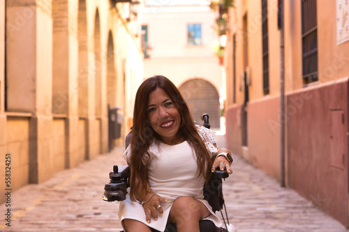 Woman with disability, reduced mobility and small stature in an electric wheelchair posing happily and flirtatiously on a city street. Concept handicap, disability, incapacity, special needs. photo