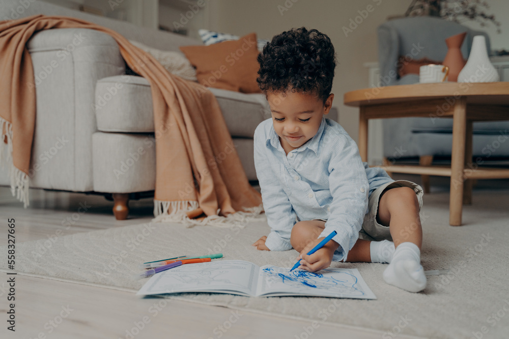 Lovely african child sitting on floor and drawing while playing at home Lovely african child sitting on floor and drawing while playing at home