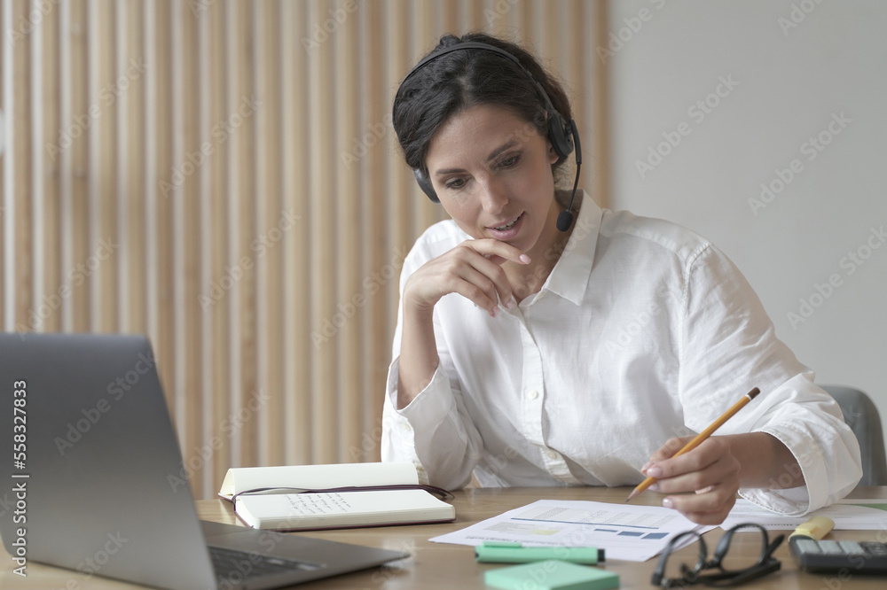 Young professional female business consultant in headset talking with client online in office Young professional female business consultant in headset talking with client online in office
