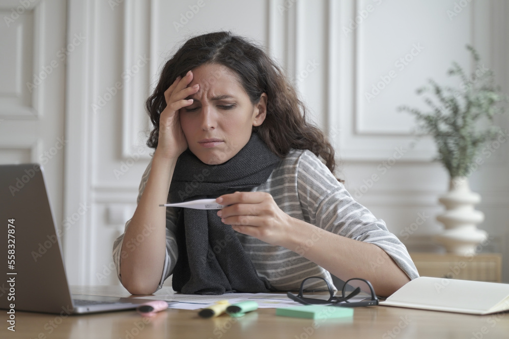 Unhealthy spanish woman wrapped in warm knitted scarf looking anxiously on digital thermometer Unhealthy spanish woman wrapped in warm knitted scarf looking anxiously on digital thermometer