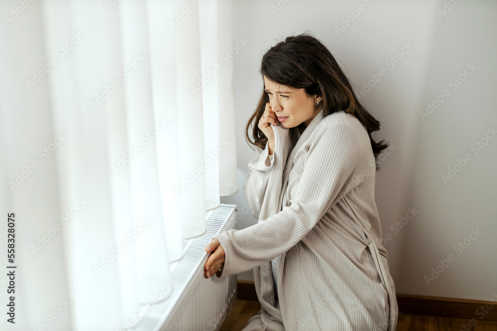 Unhappy pregnant woman is checking on cold radiator and freezing in her apartment. Unhappy pregnant woman is checking on cold radiator and freezing in her apartment.