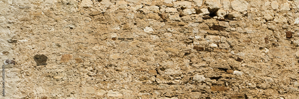 Fototapeta premium Ancient stone wall. Weathered rough masonry surface. The wall of the old castle. Wide panoramic texture for background and design.