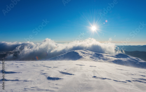 Sun and clouds over the mountains covered with snow. The mountain slope covered with ice and snow in a strong wind.