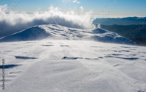 Clouds over the mountain peak. The mountain slope covered with ice and snow during snowstorm.