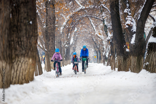 Father with children ride bikes in winter. Man with son and daughter riding bikes in winter park