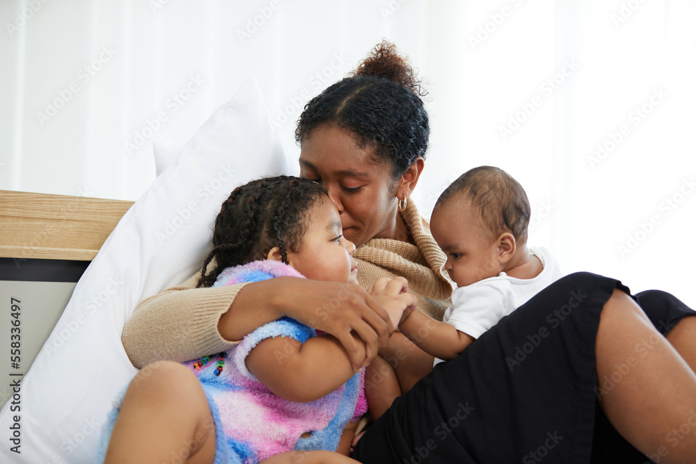 African young mother with her infant baby and kid kissing and hugging on bed African young mother with her infant baby and kid kissing and hugging on bed