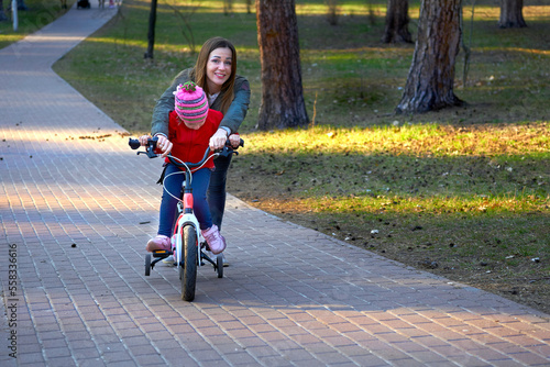 Cheerful mom teaches her child to ride a bike in autumn spring park
