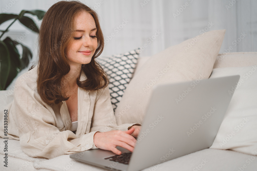 Portrait of a young redhead female freelancer sitting on the couch and using laptop at home happily. Portrait of a young redhead female freelancer sitting on the couch and using laptop at home happily.