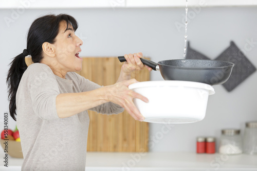 woman holding bucket while water droplets leak from ceiling