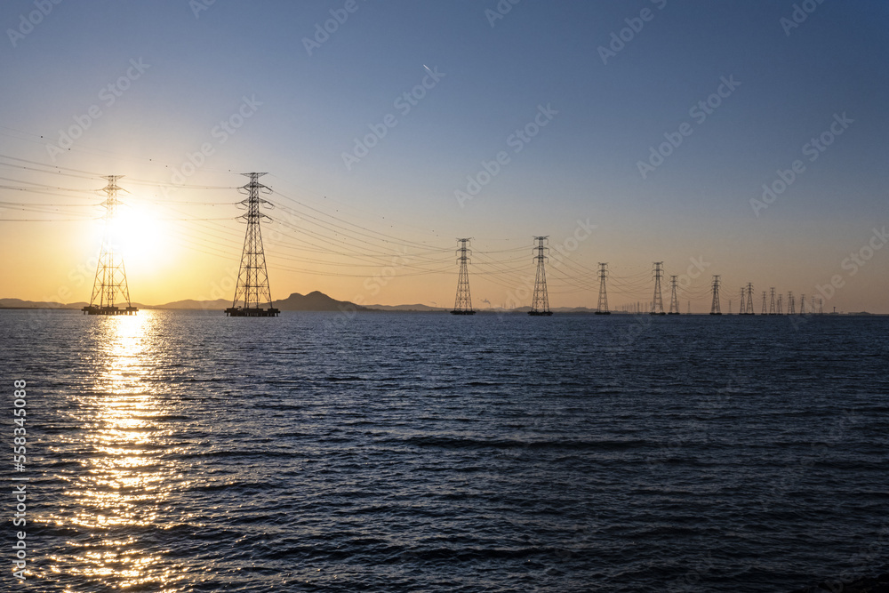 바다 위에 설치된 송전탑과 그 뒤로 떨어지는 태양