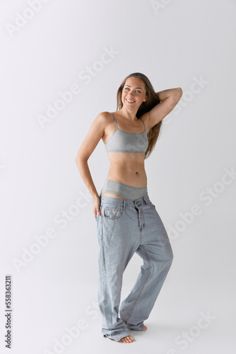 Full-length portrait of slim woman posing in top and jeans over grey studio background. Positive, smiling mood
