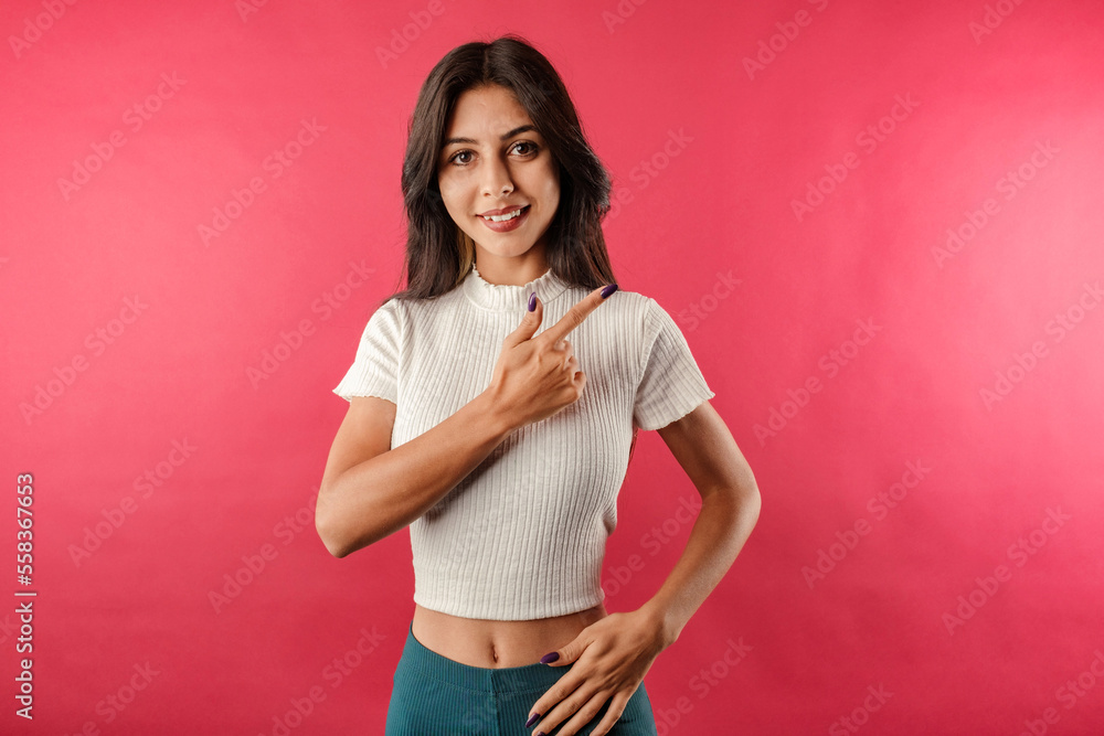 Young caucasian woman wearing casual top isolated over red background smiling face and pointing with hand and finger to the side looking at the camera. Smiling friendly. Young caucasian woman wearing casual top isolated over red background smiling face and pointing with hand and finger to the side looking at the camera. Smiling friendly.
