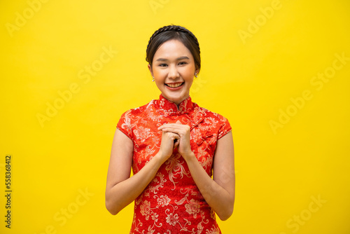 Beautiful Asian woman wearing traditional cheongsam with gesture of congratulation isolated on yellow background, Happy Chinese New Year. photo