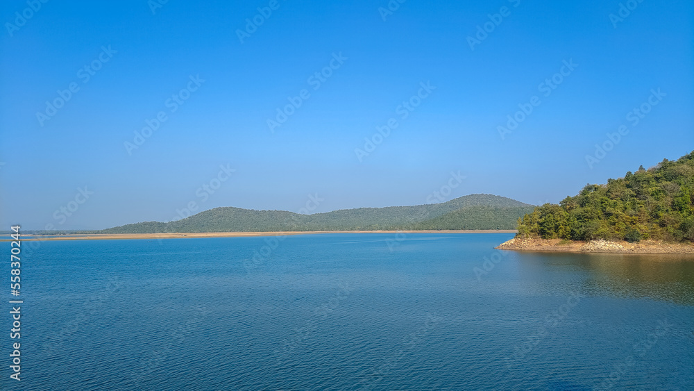 Lake with clear blue sky and green forest background, summer scene
