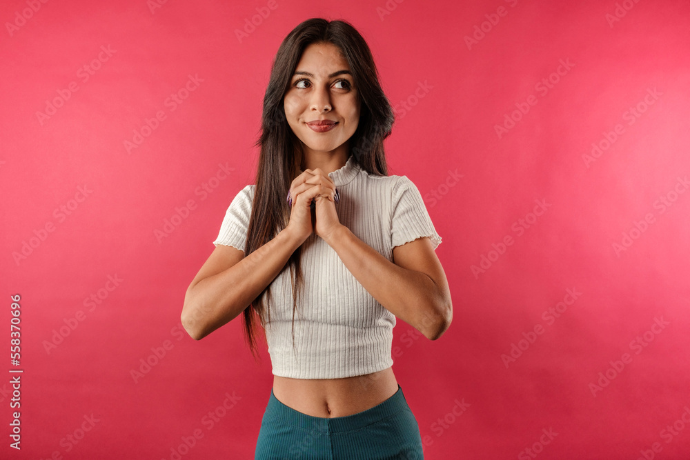 Beautiful brunette woman wearing white ribbed crop isolated over red background imagining and thinking with her hands together. Looking to empty corner copy space. Beautiful brunette woman wearing white ribbed crop isolated over red background imagining and thinking with her hands together. Looking to empty corner copy space.
