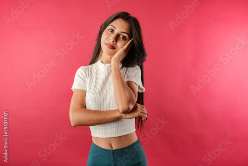 Young dark-haired woman wearing ribbed crop isolated over red background looking reluctant and unamused at camera  leaning face on hand. Listening boring person. Listens to lies and does not believe.