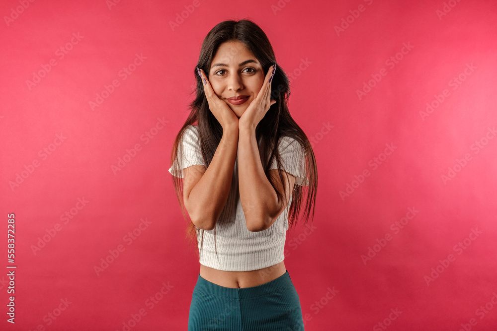 Cute dark-haired woman wearing casual top isolated over red background touch palms cheeks look you enjoy. Touching chin with palms, looks lovingly at the camera, at you. Cute dark-haired woman wearing casual top isolated over red background touch palms cheeks look you enjoy. Touching chin with palms, looks lovingly at the camera, at you.