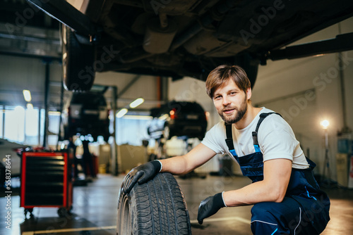 Car service, repair, maintenance and people concept. Portrait of young adult male mechanic changing a wheel of a modern car.