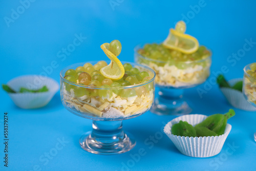 meat chicken salad in layers in a transparent glass with green grapes and lemon slices next to kiwi on a blue background. for labels, screensavers, business cards, banners, menu signs