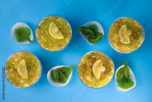 meat chicken salad in layers in a transparent glass with green grapes and lemon slices next to kiwi on a blue background. for labels, screensavers, business cards, banners, menu signs