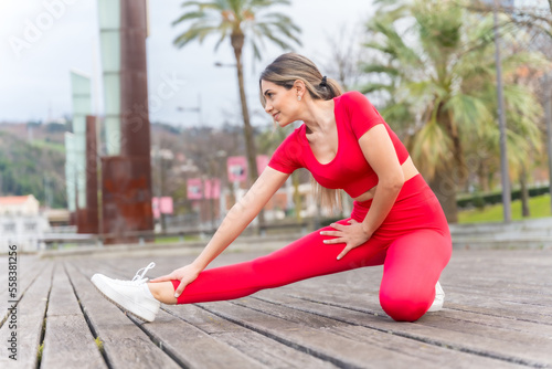 Fit woman in red clothes doing stretching in a city park in spring, fitness