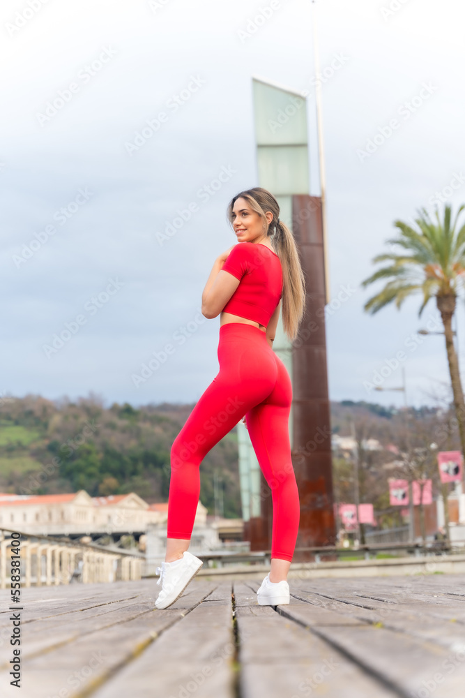 Portrait of young fit woman in red clothes doing sports in the city in spring, fitness