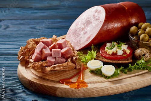 Sausage cut into slices and cubes on a wooden board with bread, vegetables, herbs, sauce, eggs on a blue wooden table