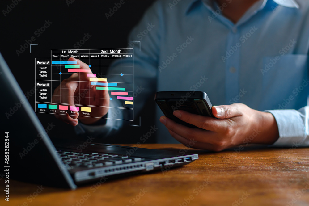 Project manager working on tablet and updating tasks and milestones progress planning with Gantt chart scheduling interface for company on virtual screen. Business Project Management System. Project manager working on tablet and updating tasks and milestones progress planning with Gantt chart scheduling interface for company on virtual screen. Business Project Management System.