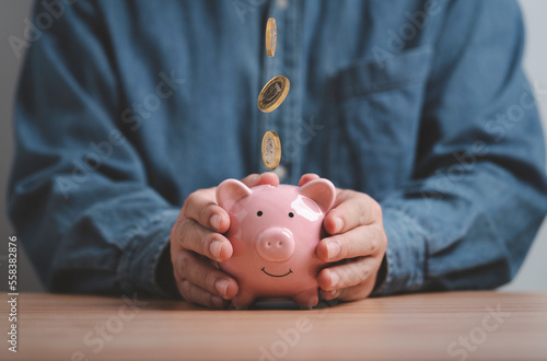 Businessman holding pink piggy deposit bank which coins dropping for money saving to investment and get dividend return concept.