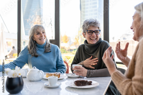 Group of elderly women have breakfast in a cafeteria  three retired female friends are celebrating an anniversary drinking tea and coffee and eating chocolate cakes