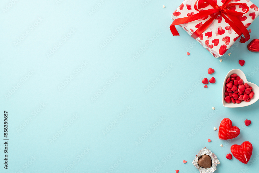 Valentine's Day concept. Top view photo of present box heart shaped saucer with sprinkles candies and candles on isolated light blue background with copyspace Valentine's Day concept. Top view photo of present box heart shaped saucer with sprinkles candies and candles on isolated light blue background with copyspace