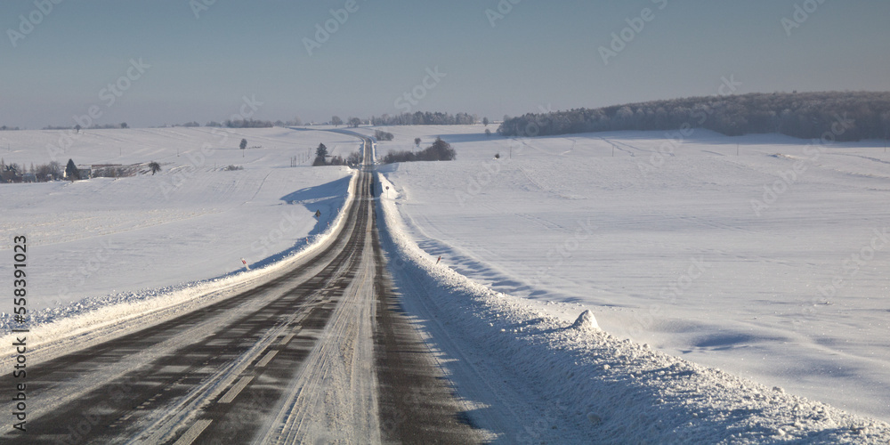 Winter road. Winter landscape of road. Snowy winter on the countryside, black and white picture. Highway leading through snowy fields. Drifts on the road.