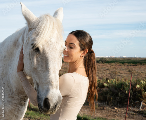 Young happy woman embracing his horse. Person cuddleling wild animal in open field grass.