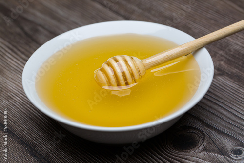 Honey with honey dipper in white bowl on wooden background.