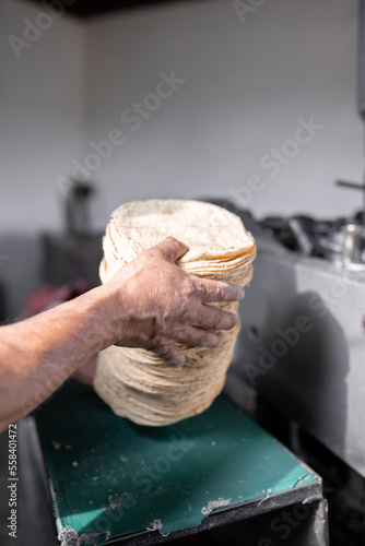 An adult tortilla maker is picking up a pile of baked corn tortillas ready to sale photo