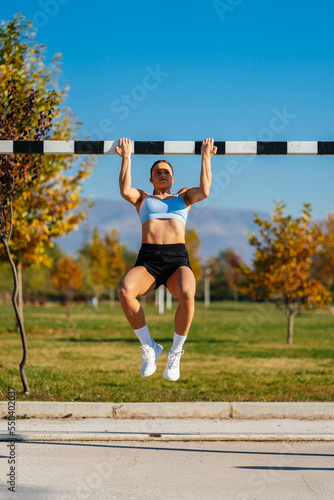 Strong fit girl doing pull ups while holding the goal's crossbar. Working out in the park